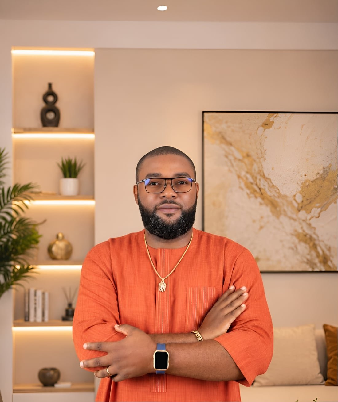 Reuben Ugbine Karo, visual artist, standing with his arms crossed in front of a large gold and cream abstract painting